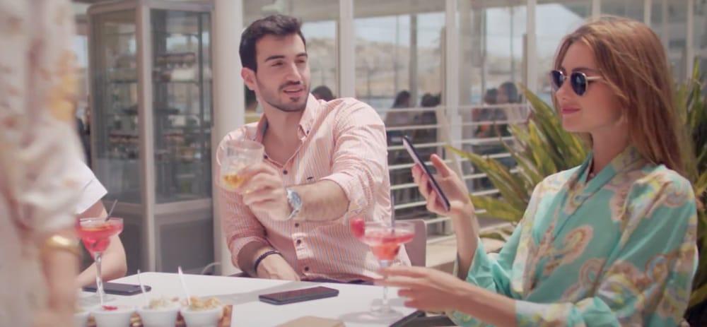 Two young ladies and a young man sit at a table having a drink in motion blur's commercial